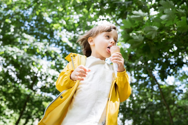 Photo enfant en bas âge mangeant de la crème glacée dans un cône à l'extérieur enfant portant une veste jaune légère grignotant dans le parc en été nourriture sucrée savoureuse