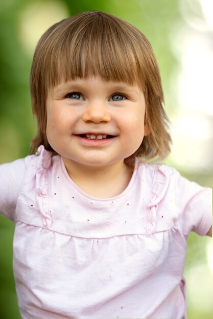 Enfant en bas âge mignon, bébé souriant sur fond vert estompé. Belle petite fille s'amusant.