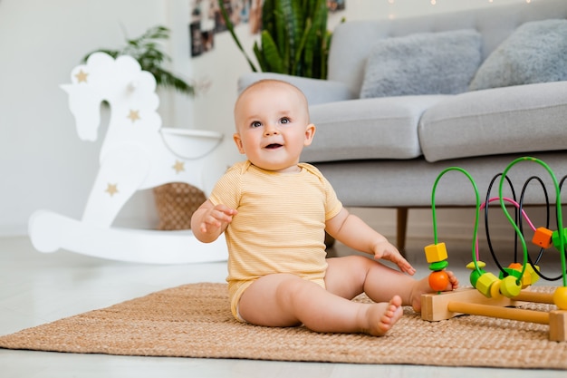Enfant en bas âge mignon en body jaune est assis à la maison sur le sol en jouant dans un jouet en développement. concept de développement de l'enfant