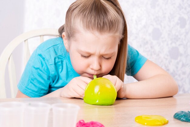 Un enfant blond gonfle une bouteille de slime jaune