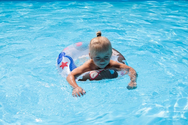 Une enfant blonde joue à nager avec un anneau gonflable dans une piscine d'été