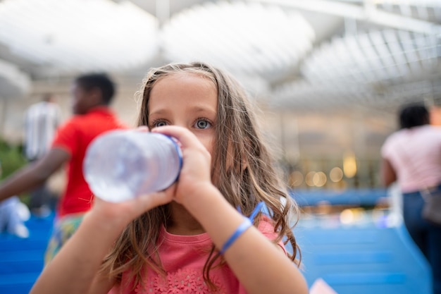 Un enfant boit de l'eau d'une bouteille en plastique à l'extérieur