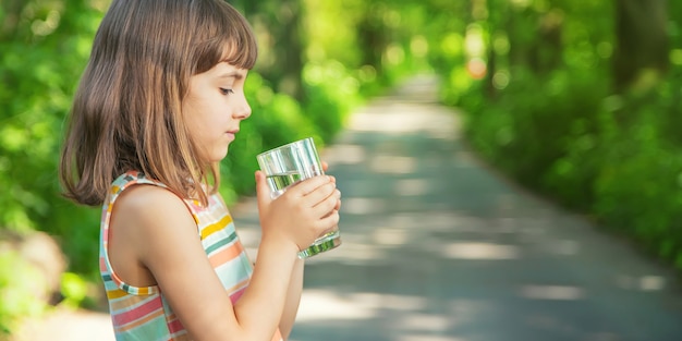 Un enfant boit de l'eau dans un verre sur la nature