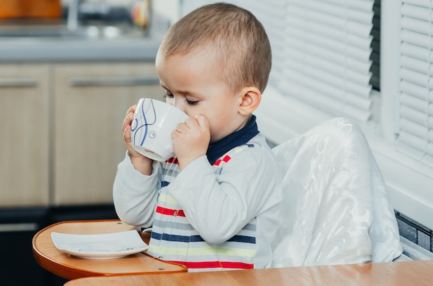 Un enfant boit une tasse de thé, café, cacao, cuisine à domicile