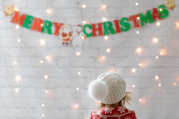 Enfant en bonnet blanc avec pompon look à guirlande Joyeux Noël