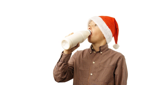 Enfant en bonnet de Noel boit du lait dans une bouteille, isolé sur fond blanc.