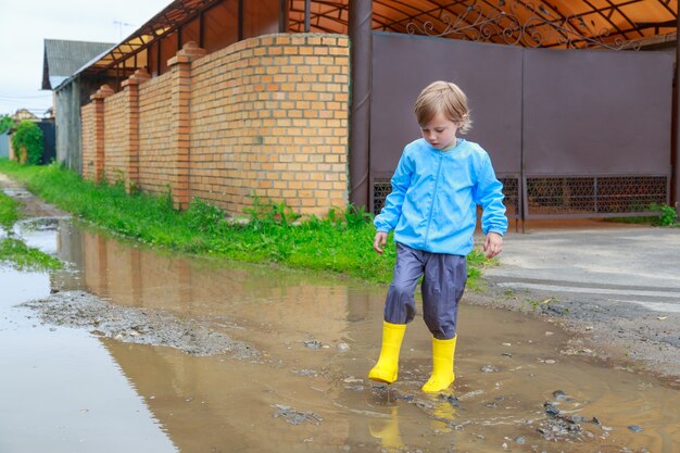 Enfant en bottes de caoutchouc et imperméable jouant dans une flaque d'eau