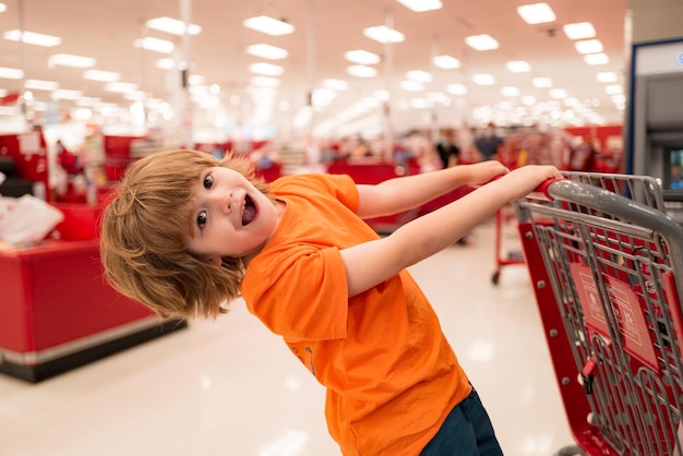 Enfant avec caddie plein de fruits et légumes biologiques frais debout dans le rayon épicerie ...