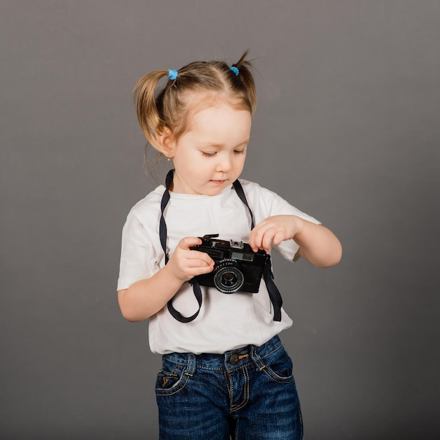 Enfant avec caméra. Petite fille photographiant en arrière-plan studio