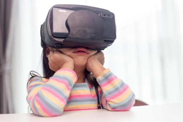 Enfant avec casque de réalité virtuelle assis derrière une table à l'intérieur à la maison