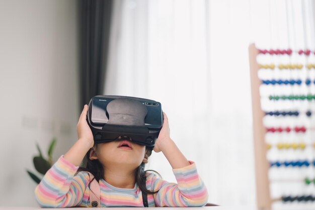 Enfant avec casque de réalité virtuelle assis derrière une table à l'intérieur à la maison