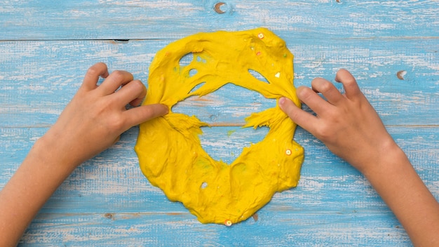 L'enfant casse le visage d'un slime jaune sur une table en bois