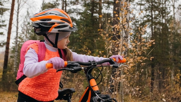 Un enfant caucasien à pied avec vélo dans le parc d'automne Petite fille marchant cycle orange noir