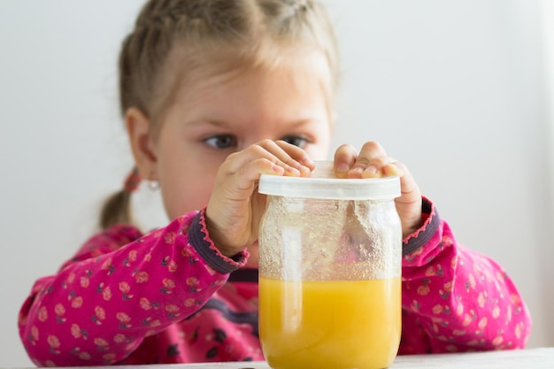 Enfant caucasien de trois ans essayant de retirer le couvercle du pot avec du miel à l'intérieur