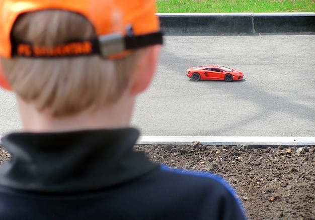 Photo enfant en chapeau orange regarde à la voiture de jouet rouge.