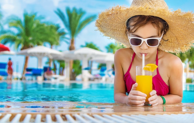 Enfant avec un chapeau de paille buvant un cocktail au bord de la piscine