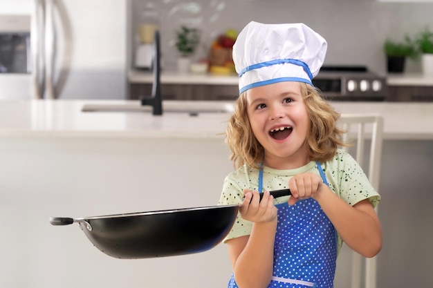 Enfant chef cuisinier cuisine avec casserole dans la cuisine Enfant en toque et tablier préparant la nourriture dans la cuisine Enfants de cuisine Enfant garçon avec tablier et toque préparant un repas sain dans la cuisine