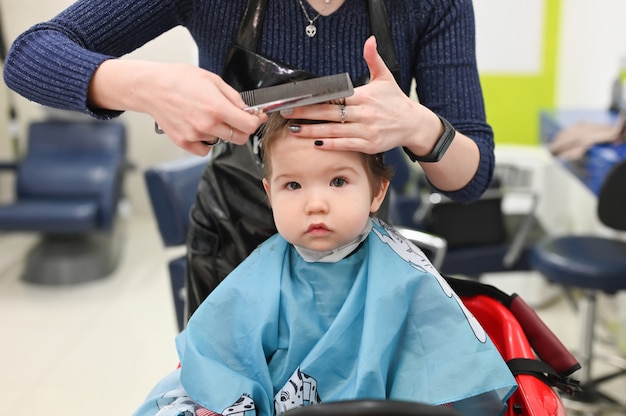 Un enfant chez le coiffeur. La première coupe de cheveux de l'enfant chez le coiffeur. Bébé coupe de cheveux enfant en bas âge.