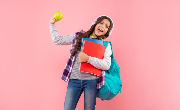 Un Enfant Choqué écoute De La Musique Dans Un Casque Avec Un Sac à Dos Avec Un Classeur Et Un Déjeuner Aux Pommes