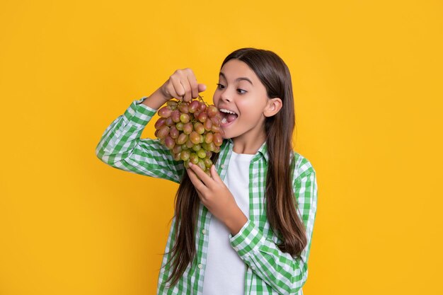 Enfant choqué avec grappe de raisins mûrs sur fond jaune