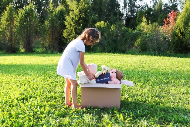 Enfant collectionnant des jouets pour la charité. Peluches dans une boîte en carton à l'extérieur.