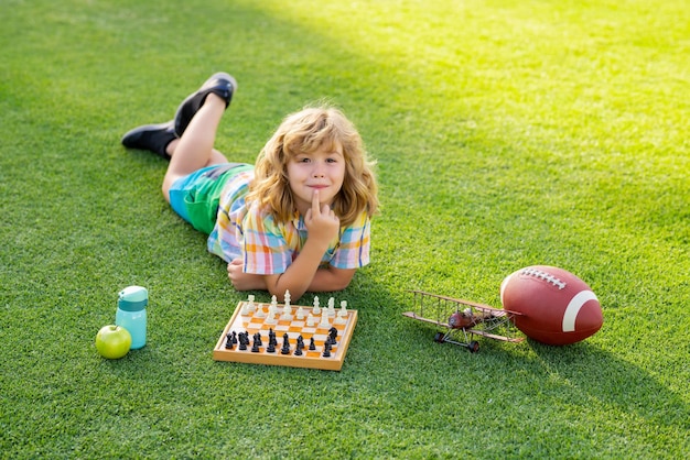 Enfant concentré développant une stratégie d'échecs jouant à un jeu de société dans l'arrière-cour allongé sur l'herbe