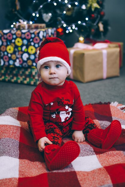 Un enfant en costume du père Noël est assis sous un arbre de Noël