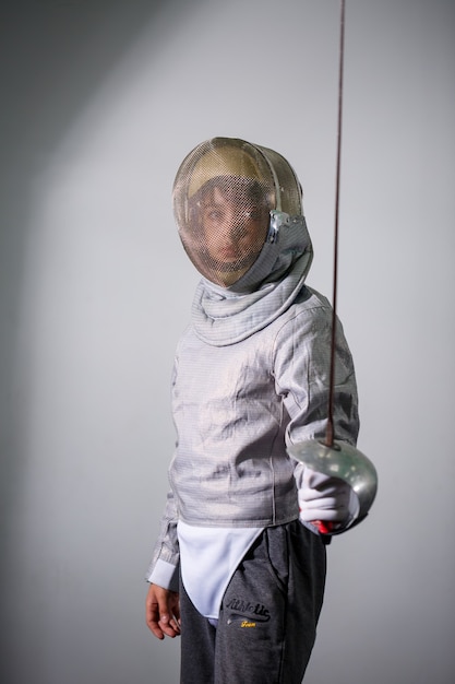 Photo enfant en costume d'escrime avec une épée à la main en studio. les jeunes filles pratiquent et pratiquent l'escrime. sport, mode de vie sain.