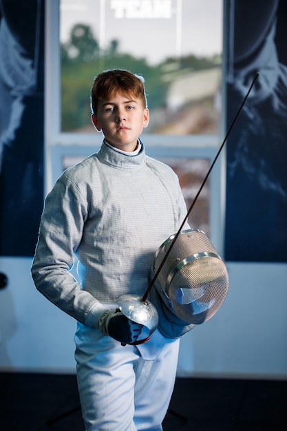 Enfant en costume d'escrime avec une épée à la main en studio. Les jeunes garçons pratiquent et pratiquent l'escrime. Sport, mode de vie sain.