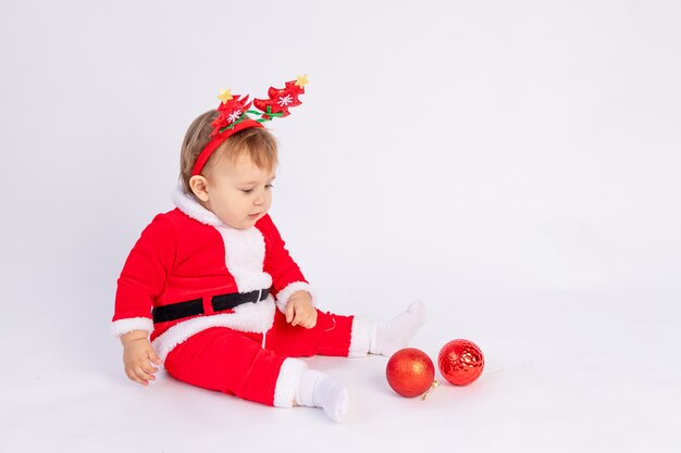 Un enfant en costume de Père Noël avec des boules de Noël rouges