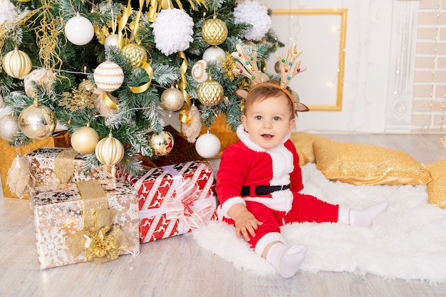 Un enfant en costume de Père Noël est assis à l'arbre de Noël avec des cadeaux, le concept du nouvel an et de Noël