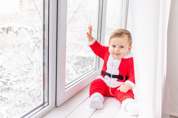 Enfant en costume de Santa sur le rebord de la fenêtre, le concept de nouvel an et de Noël