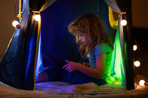 Enfant couché dans son lit et apprenant dans une classe d'école virtuelle en ligne enfant travaillant sur internet pour ordinateur portable à la maison