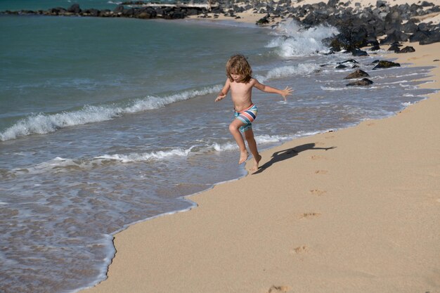 Enfant courant dans l'eau près du rivage le long de la plage de la mer un garçon court le long de la côte de la mer reste o