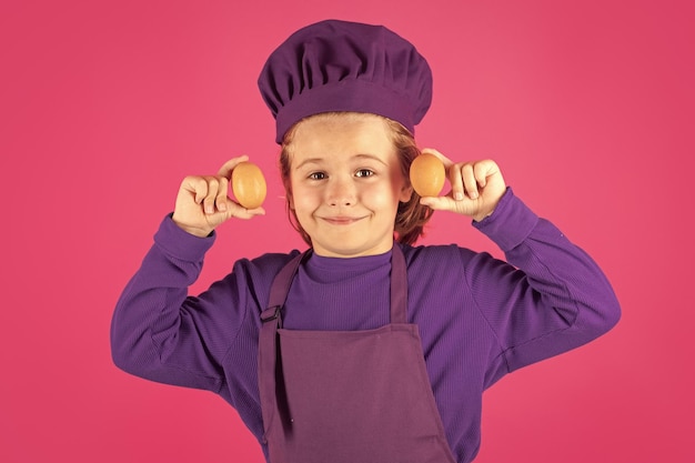 Enfant cuisinier tenant des œufs Enfant en uniforme de cuisinier Enfant chef isolé sur fond rose Enfant mignon pour être chef Enfant vêtu d'un chapeau de chef