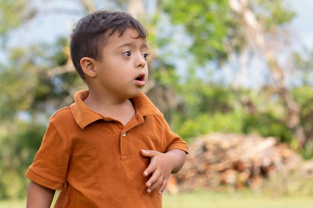 Un enfant curieux avec le syndrome de Down perdu dans ses pensées dans un cadre de campagne rustique