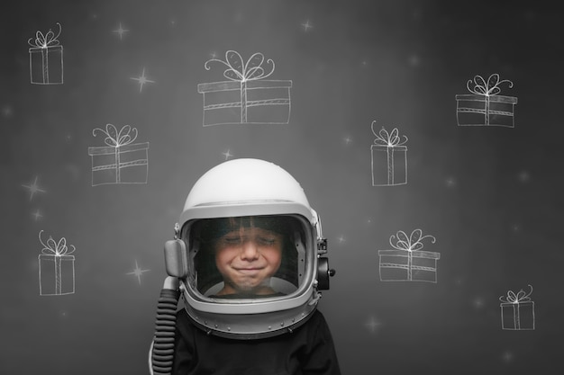 enfant dans le casque d'un astronaute rêve de Noël et cadeaux