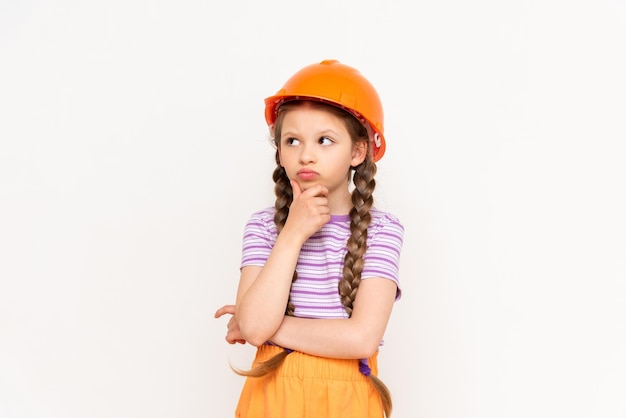 Un enfant dans un casque de construction pensait tenir son menton avec ses doigts Une petite fille avec des nattes sur un fond blanc isolé