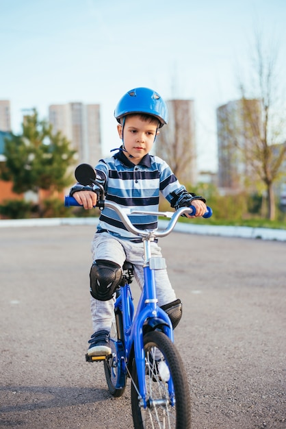 Un enfant dans un casque et une protection lors d'une balade à vélo sur la nature au printemps