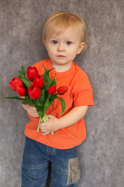 Un enfant dans une chemise orange et un jean tient des tulipes rouges en grappes