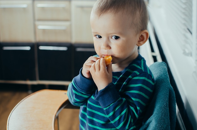 L'enfant dans la cuisine mangeant une mandarine délicieuse et juteuse, une vie saine