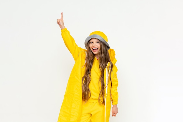 Un enfant dans un imperméable sur un fond blanc isolé Une petite fille aux cheveux longs dans un imperméable jaune et un chapeau panama