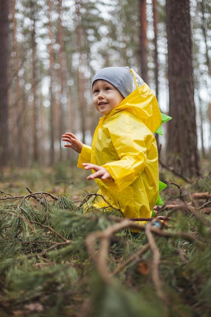 L'enfant dans l'imperméable jaune marche dans la forêt après la pluie et l'amusement