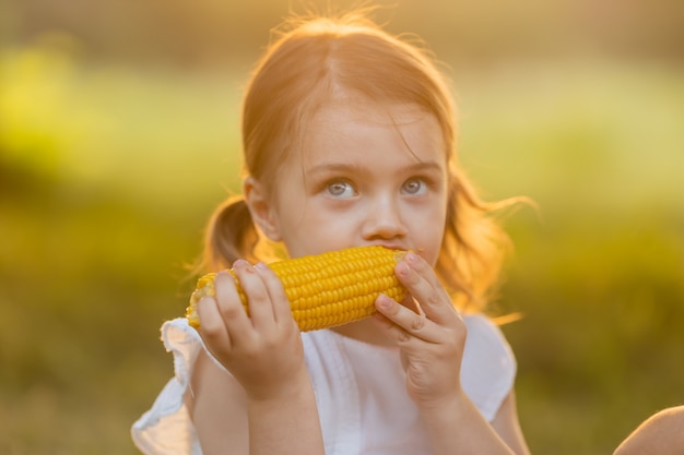 Enfant dans le jardin fille mangeant des épis de maïs Nourriture sans OGM Les enfants mangent des fruits à l'extérieur