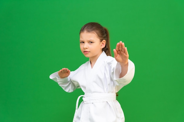 Un enfant dans un kimono blanc arts martiaux dès le plus jeune âge discipline pour enfants une fille de karaté sur fond vert compétitions d'arts martiaux