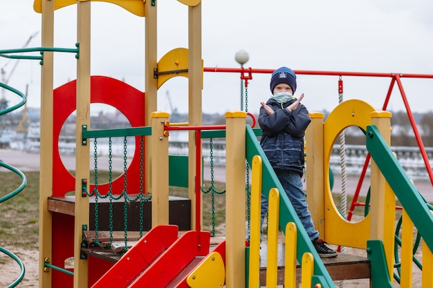 Un enfant dans un masque médical montrant un geste d'arrêt sur l'aire de jeux