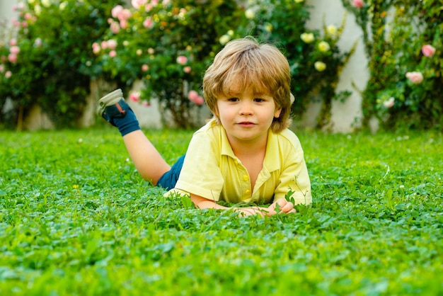 Enfant dans un parc ou un jardin extérieur. Enfant de printemps allongé sur l'herbe. Garçon d'été à pied. Adaptation des enfants.