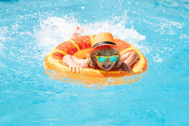 Enfant dans la piscine sur un anneau gonflable enfant nager avec un jouet d'eau flotteur orange sport de plein air sain
