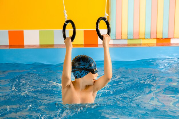 Enfant dans la piscine excersizing avec des anneaux de sport