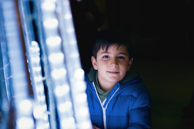 Photo enfant dans la rue souriant à côté des lumières d'un arbre à noël